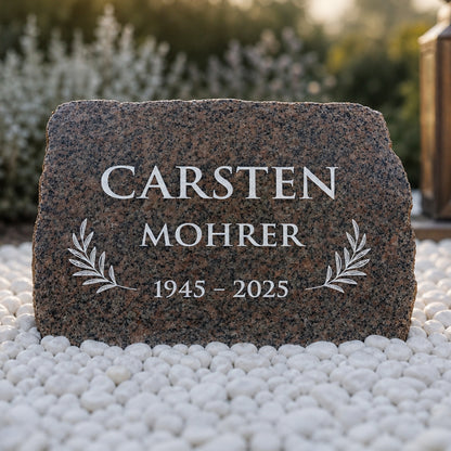 Gedenkstein aus rotem Granit mit Namen, Lebensdaten und Olivenweigen als Grabschmuck