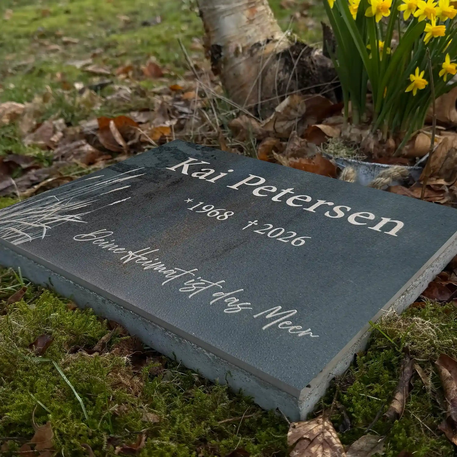 Urnengrabplatte aus Keramik mit Strandgrasmotiv und Namen, Lebensdaten und Zitat mit Betonsockel