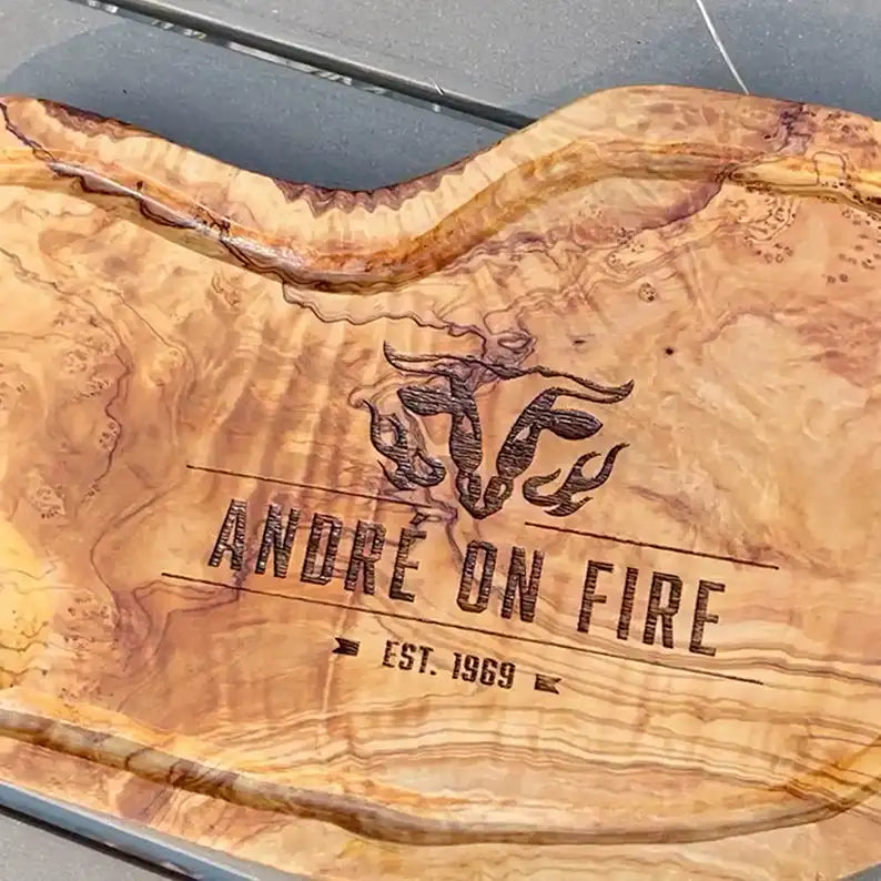 Motiv "On Fire" mit stilisiertem Rinderkopf mit Flammen und  Personaliserungsoption mit Name in Großbuchstaben und Datum - Mediterranes Schneidebrett aus Olivenholz mit Saftrille mit und ohne Grifflasche oder Handgriff - Personalisiertes Männergeschenk von Jeske Design