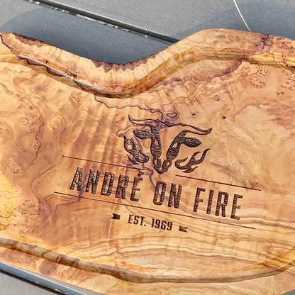 Motiv "On Fire" mit stilisiertem Rinderkopf mit Flammen und  Personaliserungsoption mit Name in Großbuchstaben und Datum - Mediterranes Schneidebrett aus Olivenholz mit Saftrille mit und ohne Grifflasche oder Handgriff - Personalisiertes Männergeschenk von Jeske Design