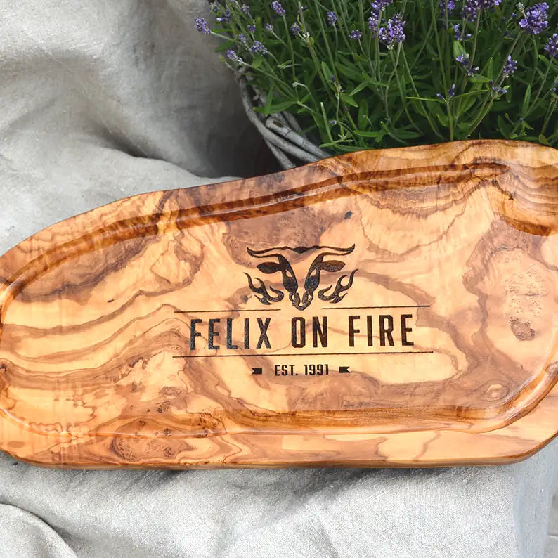 Motiv "On Fire" mit stilisiertem Rinderkopf mit Flammen und  Personaliserungsoption mit Name in Großbuchstaben und Datum - Mediterranes Schneidebrett aus Olivenholz mit Saftrille mit und ohne Grifflasche oder Handgriff - Personalisiertes Männergeschenk von Jeske Design