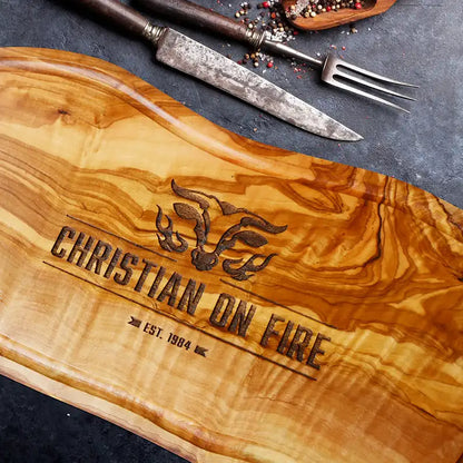 Motiv "On Fire" mit stilisiertem Rinderkopf mit Flammen und  Personaliserungsoption mit Name in Großbuchstaben und Datum - Mediterranes Schneidebrett aus Olivenholz mit Saftrille mit und ohne Grifflasche oder Handgriff - Personalisiertes Männergeschenk von Jeske Design