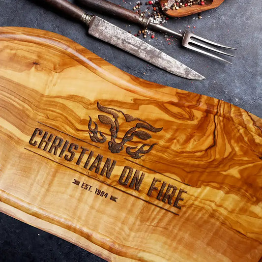 Motiv "On Fire" mit stilisiertem Rinderkopf mit Flammen und  Personaliserungsoption mit Name in Großbuchstaben und Datum - Mediterranes Schneidebrett aus Olivenholz mit Saftrille mit und ohne Grifflasche oder Handgriff - Personalisiertes Männergeschenk von Jeske Design