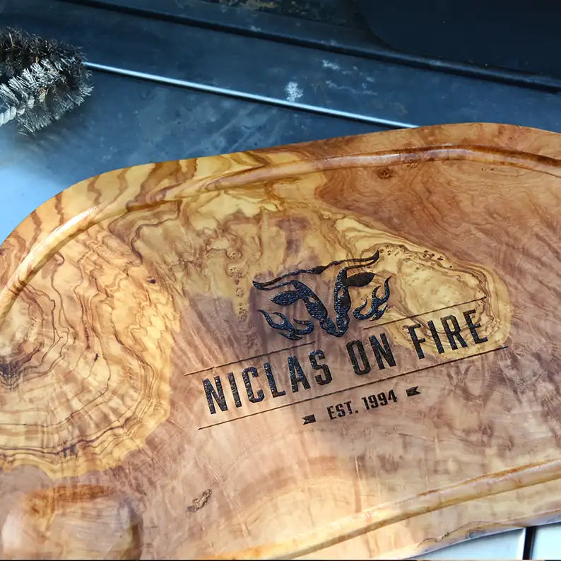 Motiv "On Fire" mit stilisiertem Rinderkopf mit Flammen und  Personaliserungsoption mit Name in Großbuchstaben und Datum - Mediterranes Schneidebrett aus Olivenholz mit Saftrille mit und ohne Grifflasche oder Handgriff - Personalisiertes Männergeschenk von Jeske Design