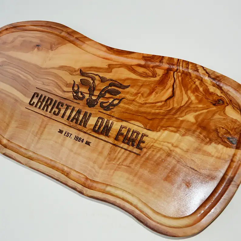Motiv "On Fire" mit stilisiertem Rinderkopf mit Flammen und  Personaliserungsoption mit Name in Großbuchstaben und Datum - Mediterranes Schneidebrett aus Olivenholz mit Saftrille mit und ohne Grifflasche oder Handgriff - Personalisiertes Männergeschenk von Jeske Design