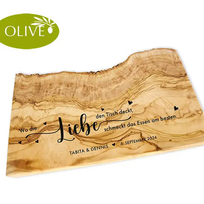 Motiv WO DIE LIEBE - Personalisiertes Schneidebrett aus Olivenholz mit rustikalem Rand und glatter Oberfläche und mit dem text "Wo die Liebe den Tisch deckt, schmeckt das Essen am besten." Darunter die personalisierten Pärchennamen und das Datum. - Jeske Design
