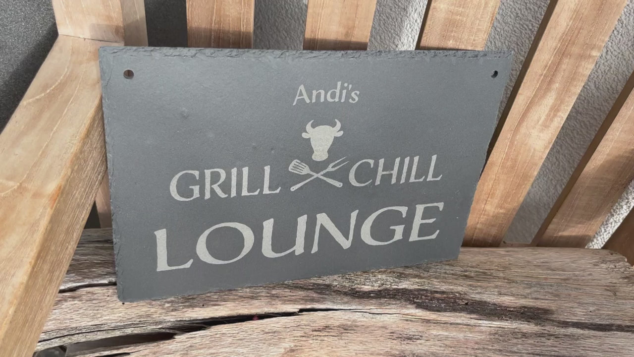 Dekoschild aus Schiefer mit dem Motiv Grill & Chill Lounge, welches auf eine Schieferplatte in der Größe 30 x 20 cm  und personalisierter Form mittels Laser graviert wird. Zwischen Grill & Chill sind gekreuzte Grillgabeln und ein stilisierter Bullenkopf.