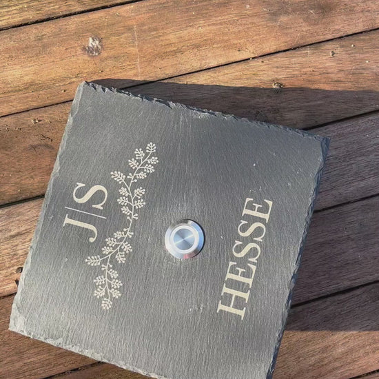 Personalisiertes Klingelschild aus Schiefer mit Taster aus Edelstahl mit LED Beleuchtung oder ohne Beleuchtung. Motiv zarter Blätterreigen mit Initialen. Name in klassischer Druckschrift unterhalb des Tasters. Klingelschild in 15x15 cm, 20x15 cm, 26x16 cm oder 30x20 cm.