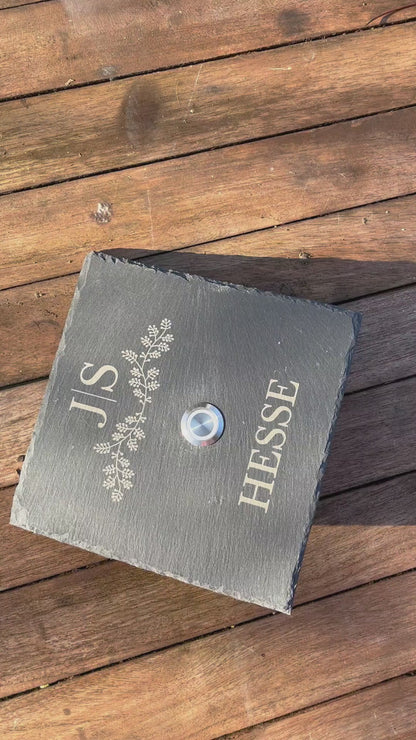 Personalisiertes Klingelschild aus Schiefer mit Taster aus Edelstahl mit LED Beleuchtung oder ohne Beleuchtung. Motiv zarter Blätterreigen mit Initialen. Name in klassischer Druckschrift unterhalb des Tasters. Klingelschild in 15x15 cm, 20x15 cm, 26x16 cm oder 30x20 cm.
