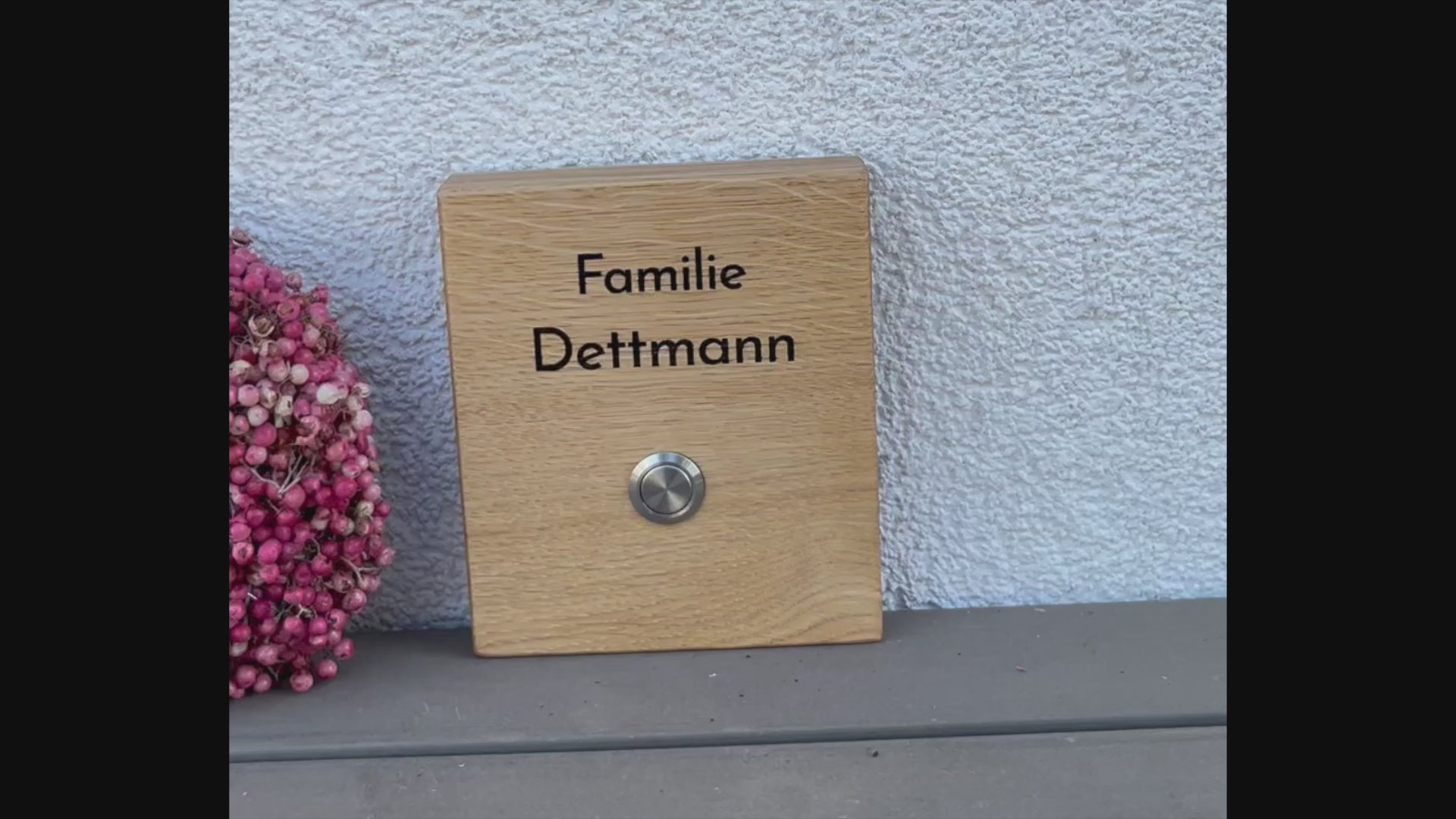 Hochwertiges Klingelschild aus Eiche in der Größe 12 x 14 cm mit moderner schlichte Schrift zweizeilig oberhalb des Tasters mit Edelstahltaster und 2 Kunststoffhalter auf der Rückseite zum Befestigen an die Hauswand